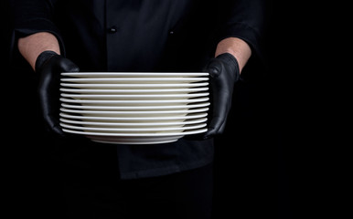 cook in black uniform holds in his hands a stack of round white empty plates
