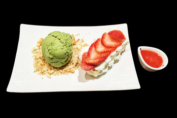 Matcha green tea ice-cream and Valentine freshness slice strawberry on whipping cream and cake. on white plate with sweet red sauce isolated on black background.
