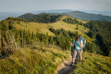 Plus size young pretty brunette woman backpacking in summer at the mountains. Outdoor activity concept. Health life and summer vacation concept. Sunny summer evening at Ukrainian Carpathians.