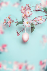 Pretty Easter background in pastel color. Spring blossom branches with pink hanging Easter egg at light blue. Easter greeting card.