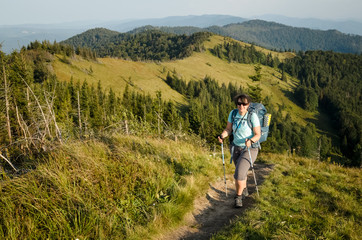 Plus size young pretty brunette woman backpacking in summer at the mountains. Outdoor activity concept. Health life and summer vacation concept. Sunny summer evening at Ukrainian Carpathians.
