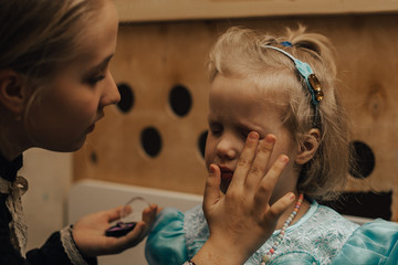 Fototapeta premium nastolatka maluje swoją młodszą siostrę makijażem