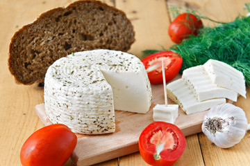 White cheese, bread, tomatoes and garlic on a wooden background