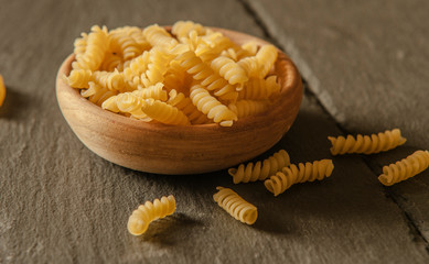 Close up of uncooked pasta in wooden bowl on tabletop in kitchen