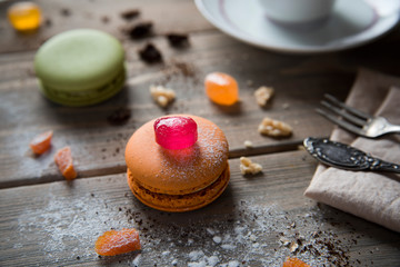 Macarons multicolored lie on a wooden table with various ingredients, chocolate, coffee, tangerines and more. Top view.