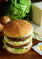 Panecillo de semillas de sésamo con, dos hambuerguesas, queso, cebolla y lechuga.