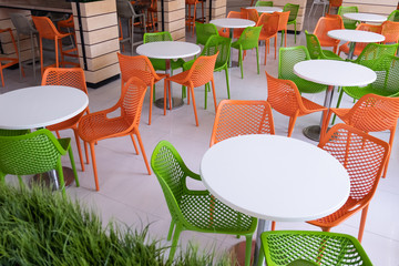 Orange and green chairs around white tables in a food court. Abstract interior in a cafe, airport or family fast food restaurant without people. Copy space.