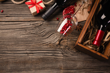 Ripe pomegranate fruit with a glass of wine, a bottle and a gift on a wooden background