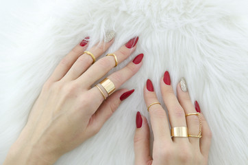 Woman hands with red nail art and jewelry on fur background.