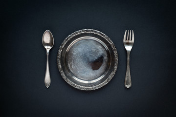 Metal antique plate, spoon and fork, on a black background