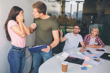 Young brunette keep face closed with hands. She is afraid of guy standing besides her. He is angry...