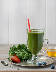 Healthy green smoothie with kale, strawberries, blueberries and honey in bottle with label on rustic wood background. Copy space.