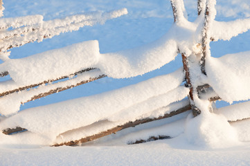 Old wooden fence covered with snow. Winter landscape in Finland.