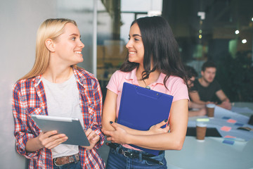 Picture of young blonde and brunette models stand together and smile. They look happy. Young women...