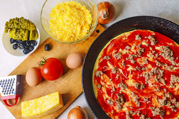 The process of cooking pizza. The view from the top. Pizza ingredients on the table with semi-finished products. Dough, tomato, eggs, cheese, olives, pickled cucumber