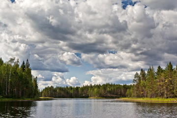 Beautiful volumetric clouds on a sunny day over a quiet forest lake