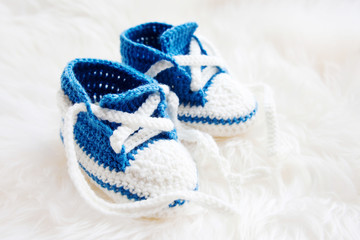 Little baby shoes. Handknitted first sneakers for newborn boy or girl. Crochet handmade bootees on fluffy white background.