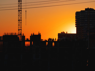 Construction of residential building. Builders go on the unfinished floor with protruding fittings. Silhouettes of workers on the background of an orange sunset.