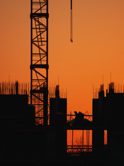 Construction of residential building. Unfinished floor with protruding fittings. Silhouettes of walls on the background of an orange sunset.
