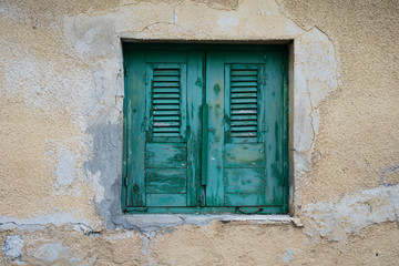 Window with turquoise shutters and blinds on the background wall of the yellow sandstone.