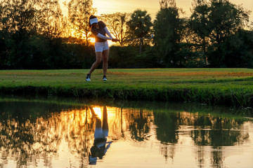 Healthy Sport. Asian Sporty woman golfer player chips and swing golf on the green sunset evening time, she presumably does exercise.  Healthy Lifestyle Concept.