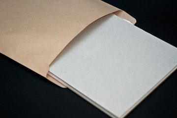 Sketchbook with a hard cardboard cover and spring pad in a craft envelope on black background. Close-up.