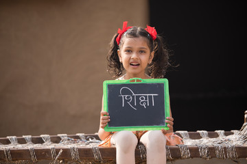 Rural Indian little girl holding slate at home