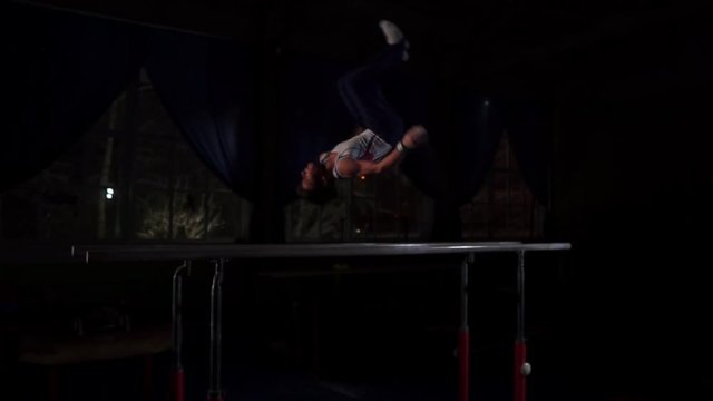 Male gymnast acrobat performs handstand on parallel bars in a dark room in slow motion