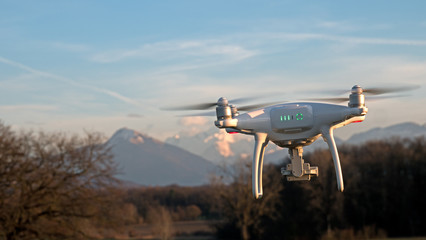 Naklejka na ściany i meble A drone hovers in flight in front of the mountains of the alps in France. The drone is stationary hovering above the ground as mountains appear in the distance.