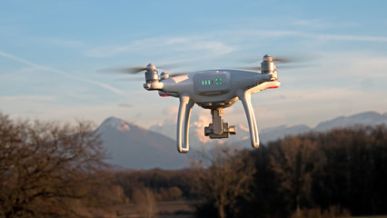A drone hovers in flight in front of the mountains of the alps in France. The drone is stationary hovering above the ground as mountains appear in the distance.