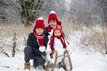 Fototapeta na wymiar Cute little toddler boy and his older brothers, playing outdoors with snow on a winter day