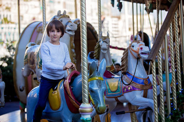 Sweet boys, brothers, riding in a Santa Claus sledge on a merry-go-round, carousel attraction in...