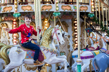 Sweet boys, brothers, riding in a Santa Claus sledge on a merry-go-round, carousel attraction in...