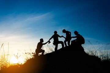 Fototapeta na wymiar friends helping each other and with teamwork trying to reach the top of the mountains during wonderful summer sunset.