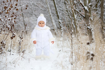 Cute little toddler boy and his older brothers, playing outdoors with snow on a winter day