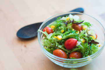 A fresh and healthy salad made with fruits and vegetables in a bowl on a wooden background.