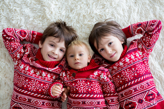 Happy brothers, baby and preschool children, hugging at home on white blanket, smiling