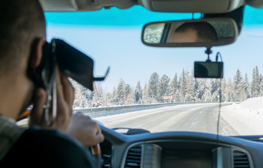 Caucasian man talking on the phone while driving a car on a slippery snow covered road in the taiga