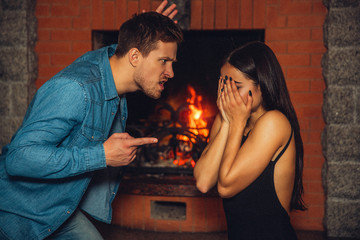 Mad young man point on woman. He look angry. Guy wave with other hand. Young woman is scared. She hides face with hands.