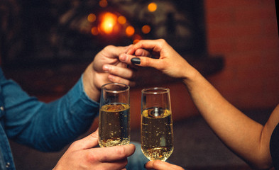 Close up of man's hand hold woman's. They also have glasses of champaigne. People sit at fireplace.