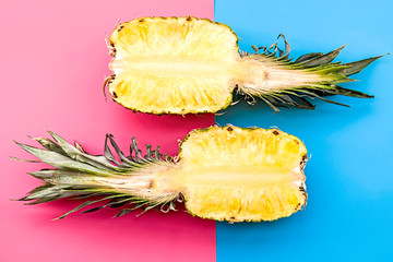 two halves of a pineapple on pink and blue background top view flat lay