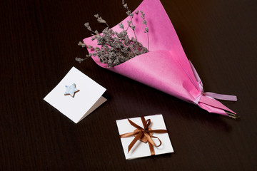 A bouquet of dried flowers, wrapped in colored paper. Near a small greeting card. On a dark background.