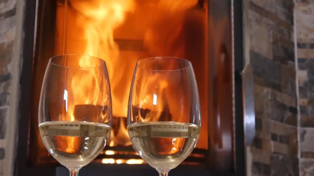 Glasses of white wine stand near the burning fireplace