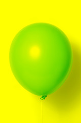 Green balloon on yellow background with shadow. Side glare.