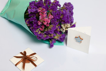 A bouquet of dried flowers, wrapped in colored paper. Near a small greeting card. On a white background.