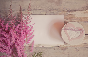 Pink astilbe flowers, gift box and empty card for your text on aged wooden background