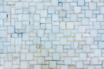 Wall lined with small bright ceramic or marble tiles, texture