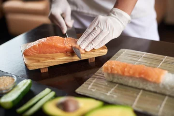 Papier Peint photo Bar à sushi Vue rapprochée du processus de préparation de délicieux sushis roulants au restaurant. Mains féminines dans des gants jetables pour trancher le saumon.