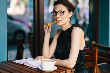 Young stylish woman with stylish glasses sitting at table in caf