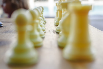 White defocused chess pieces and wooden board.
